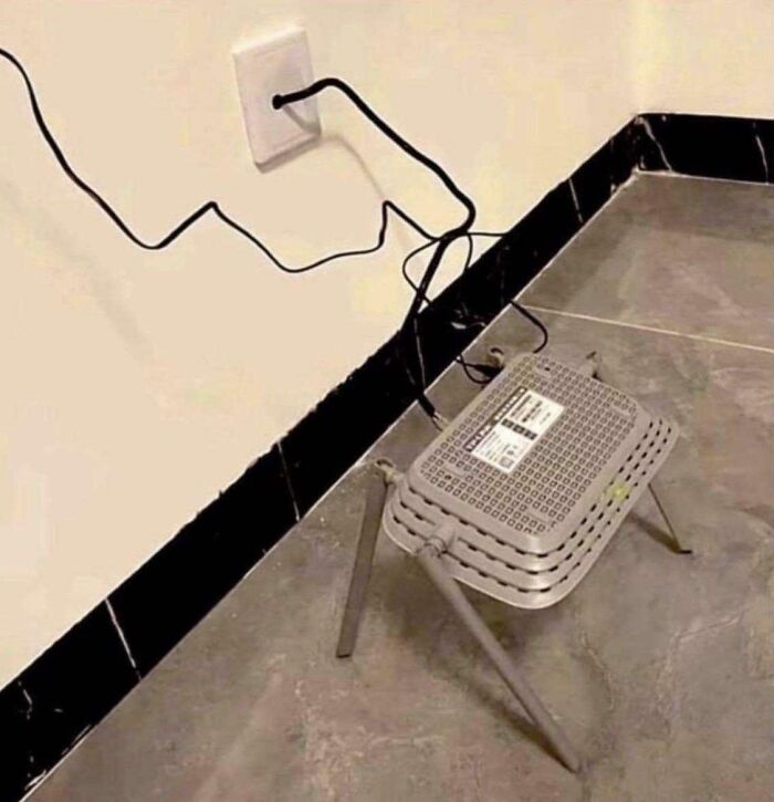 Modem placed on a small folding stool with tangled cables plugged into a wall outlet on tiled floor.