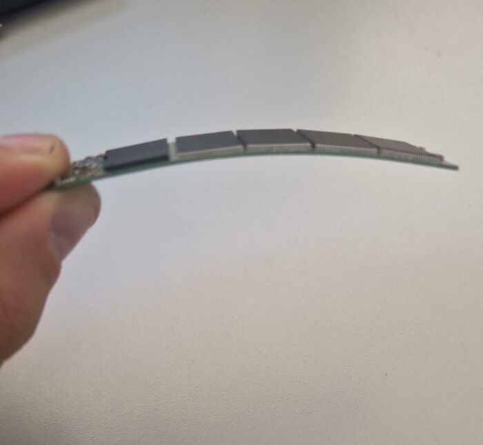 Hand holding a severely warped computer RAM module, illustrating tech support workers’ hardware troubleshooting challenges.