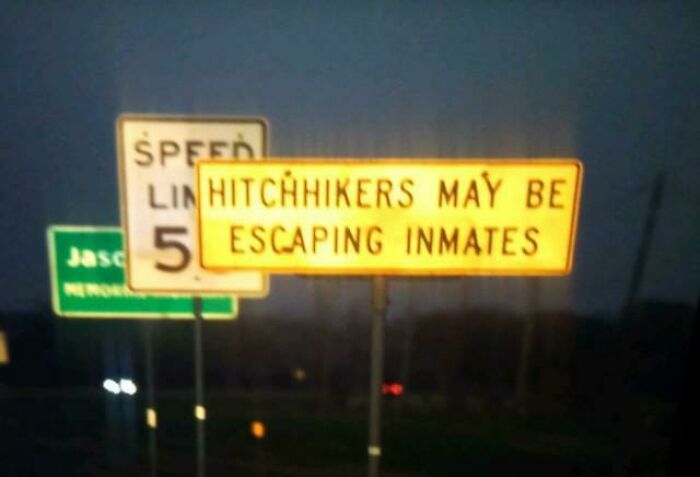 Road warning sign at night stating hitchhikers may be escaping inmates, one of the scariest signs spotted.