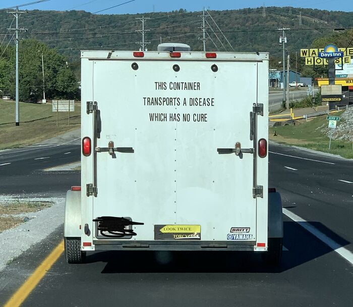 White trailer on road with scary sign warning about a disease with no cure, part of scariest signs ever spotted in the wild.