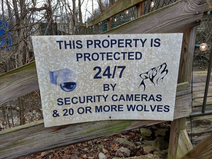 Warning sign on wooden fence about property protection with security cameras and wolves, a scary sign spotted in the wild