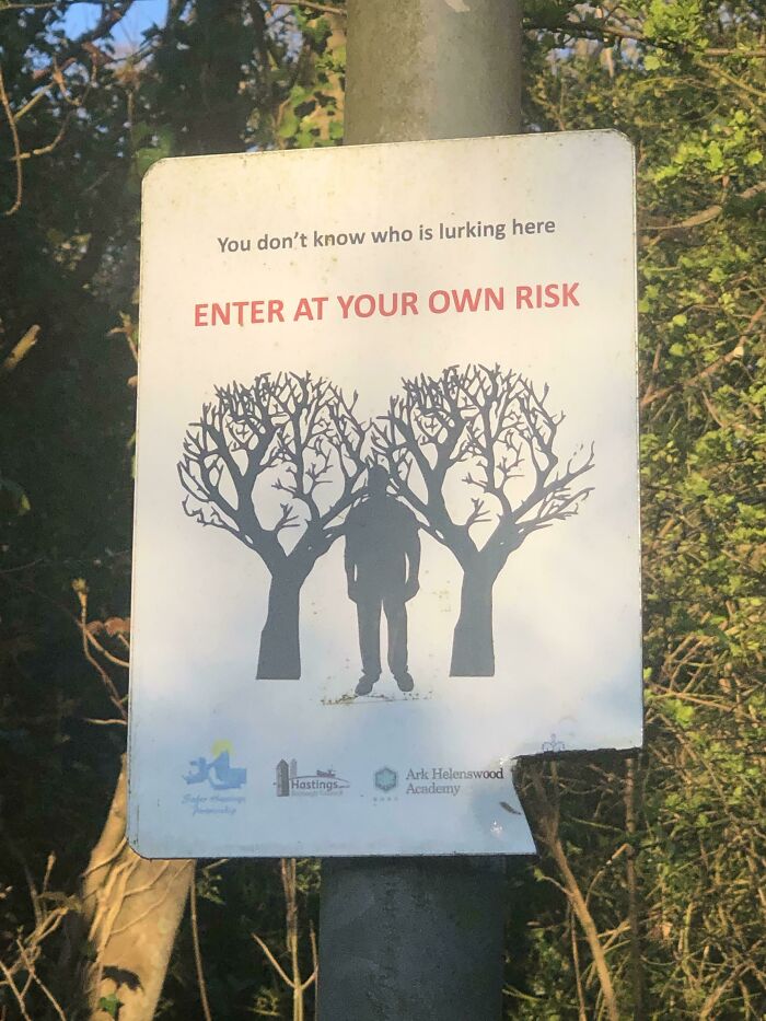 Warning sign in a wooded area showing a shadowy figure between trees with text to enter at your own risk, relating to hitchhikers.