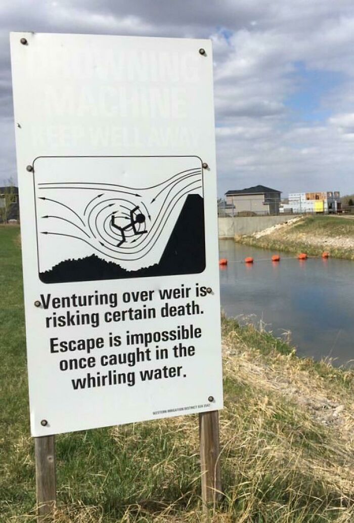 Warning sign by river showing whirling water danger, highlighting risks of venturing over weir and escaping inmates alert.