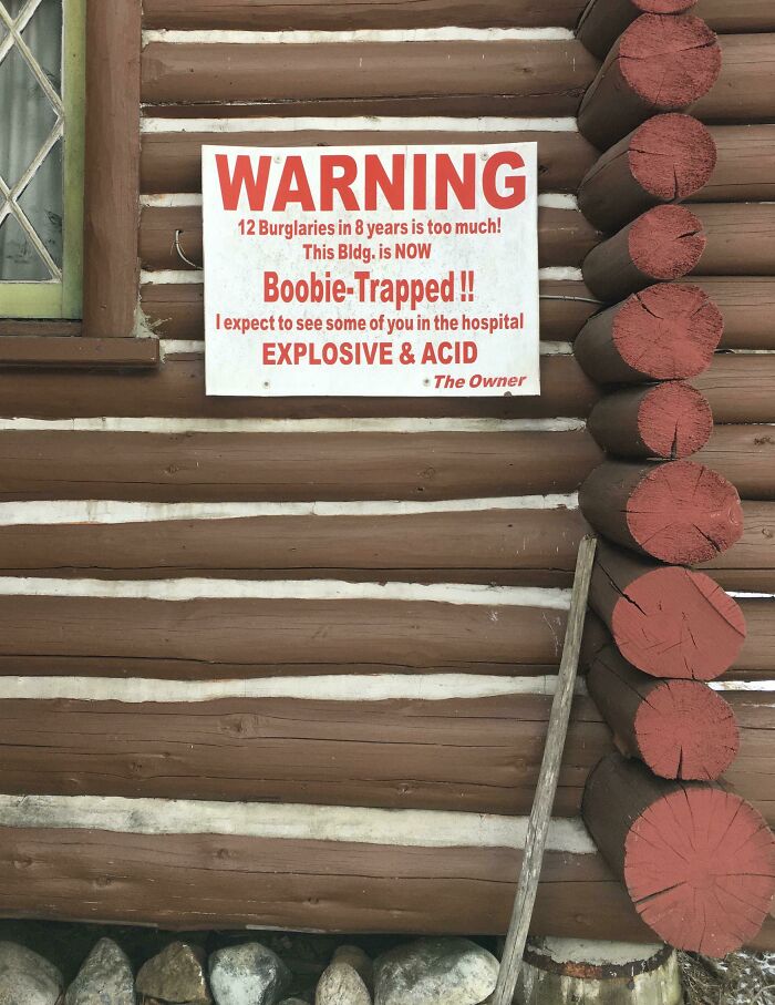 Warning sign on log cabin wall threatening explosive and acid boobie trap to deter burglars, one of the scariest signs ever spotted in the wild.