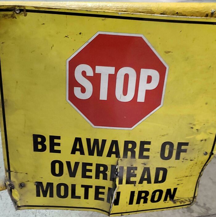 Warning sign with stop symbol and text about overhead molten iron, one of the scariest signs spotted in the wild.