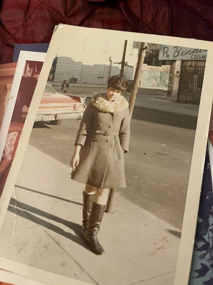 A candid old photo of a stylish woman in a coat with a fur collar and boots, holding a cigarette on a city street, revealing what the world looked like generations ago.