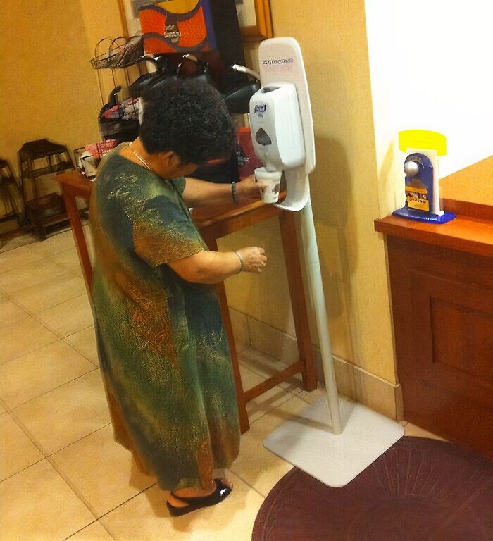 Older woman struggling to use a touchless hand sanitizer dispenser, highlighting boomers and technology fails.