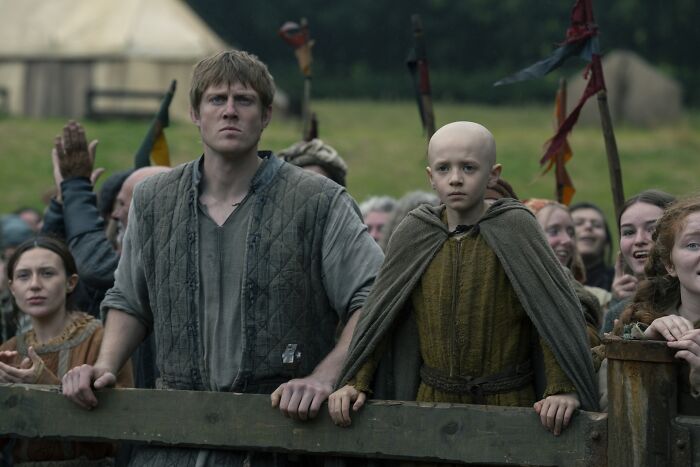 Young child star with shaved head reacting emotionally while surrounded by a crowd in a medieval setting, related to Egg role.