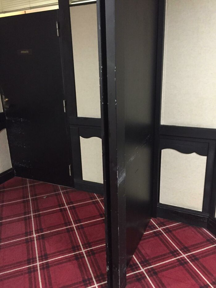 Black door in a hallway with red plaid carpet partially blocking another door, showing an architect fail with doors that lead nowhere.