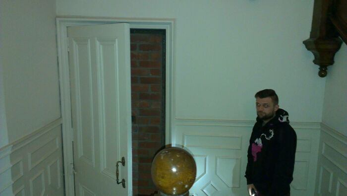 Man standing next to an interior door leading to a brick wall, illustrating architects failing with doors that lead nowhere.