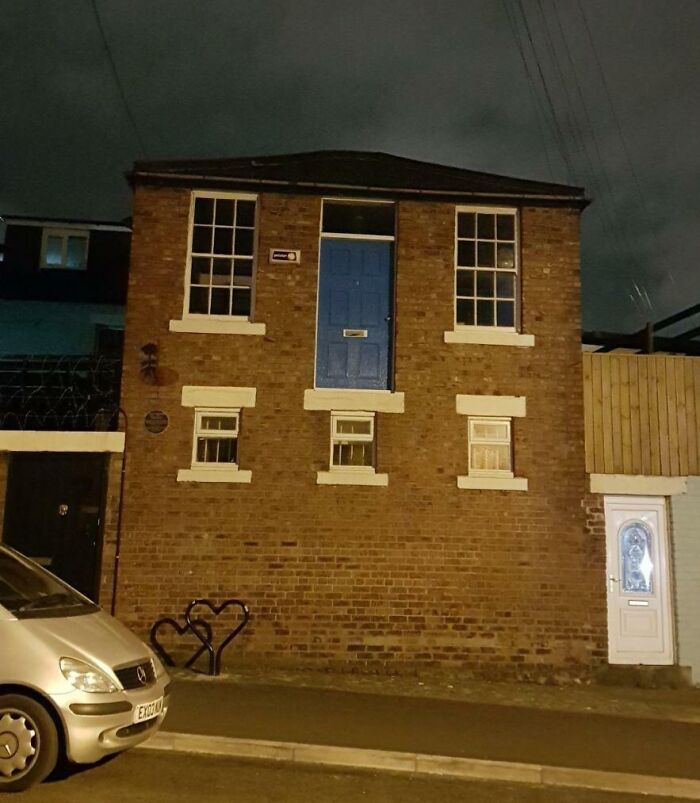 Blue door on second-story brick wall with no stairs or balcony, showcasing architects failing at designing doors that lead nowhere.
