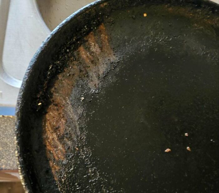 Cast iron pan with burnt and sticky residue showing a partner’s most ridiculously frustrating habits cleaning cookware.