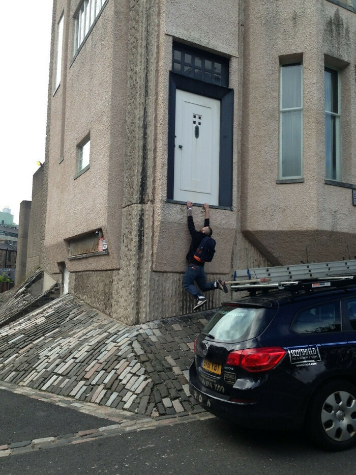 Man hanging from a door that leads nowhere on a rough concrete building, showcasing architectural design failure.