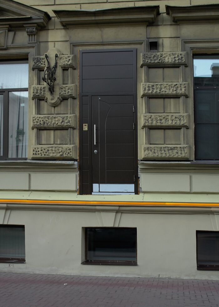 Architectural fail showing a modern door on an upper wall with no stairs or balcony, leading absolutely nowhere.