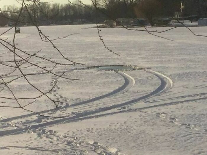 Tire tracks curving over snowy frozen lake surface with footprints nearby in a funny photo snapshot.