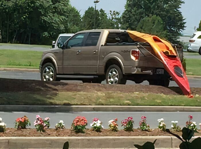 Brown pickup truck parked with a kayak awkwardly hanging off the back, a funny photo that says it all instantly