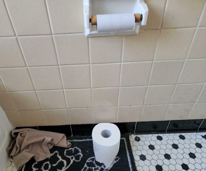 Empty toilet paper dispenser on bathroom wall with a full roll placed on the floor showing a frustrating partner habit.