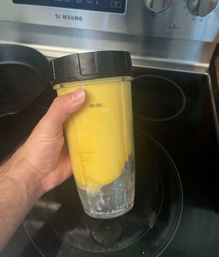 Hand holding a blender cup with a yellow smoothie under the max fill line, showing a frustrating habit in the kitchen.