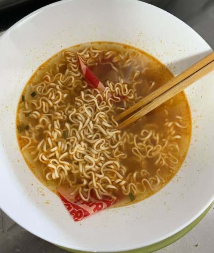 Bowl of ramen with unopened seasoning packet soaking in broth, illustrating a partner’s frustrating habit.