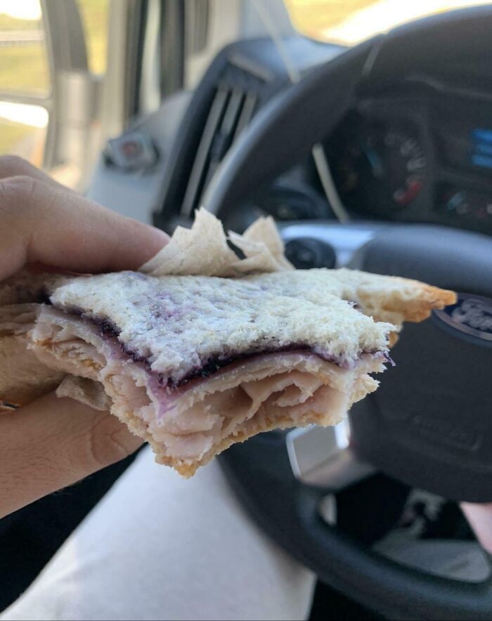 Hand holding a sandwich with uneven layers of turkey and jelly inside a car, illustrating frustrating partner habits.