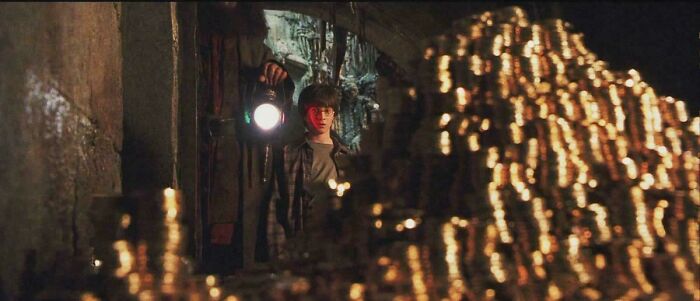 A young man holding a lantern in a dark room filled with stacks of gold coins, showcasing absurd movie details.