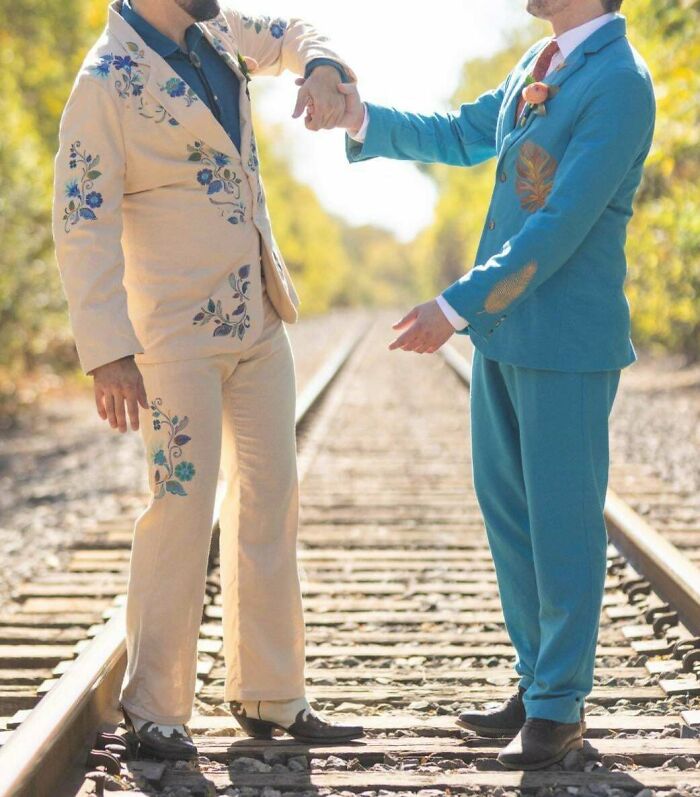 Two men wearing colorful suits on railroad tracks, showcasing their unique DIY fashion wins outdoors.