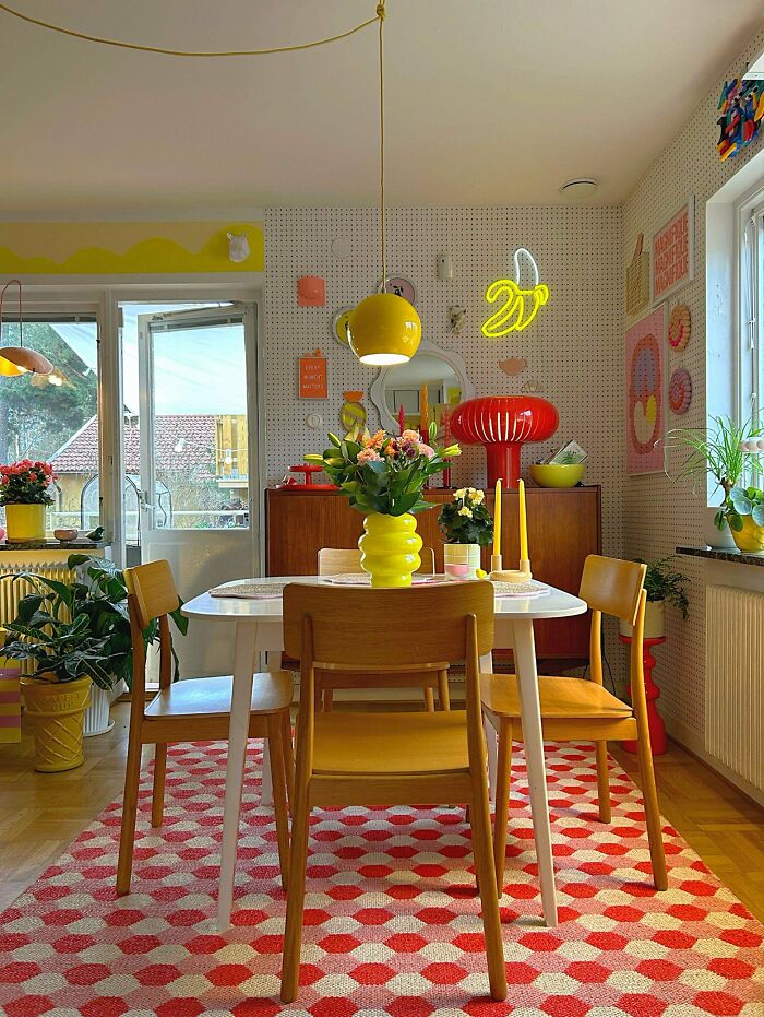 Bright dining room with colorful decor, patterned rug, vibrant plants, and eclectic wall art embracing more is more home style.
