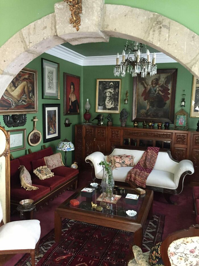Eclectic living room embracing more is more style with vintage furniture, ornate decor, and numerous framed artworks on green walls.