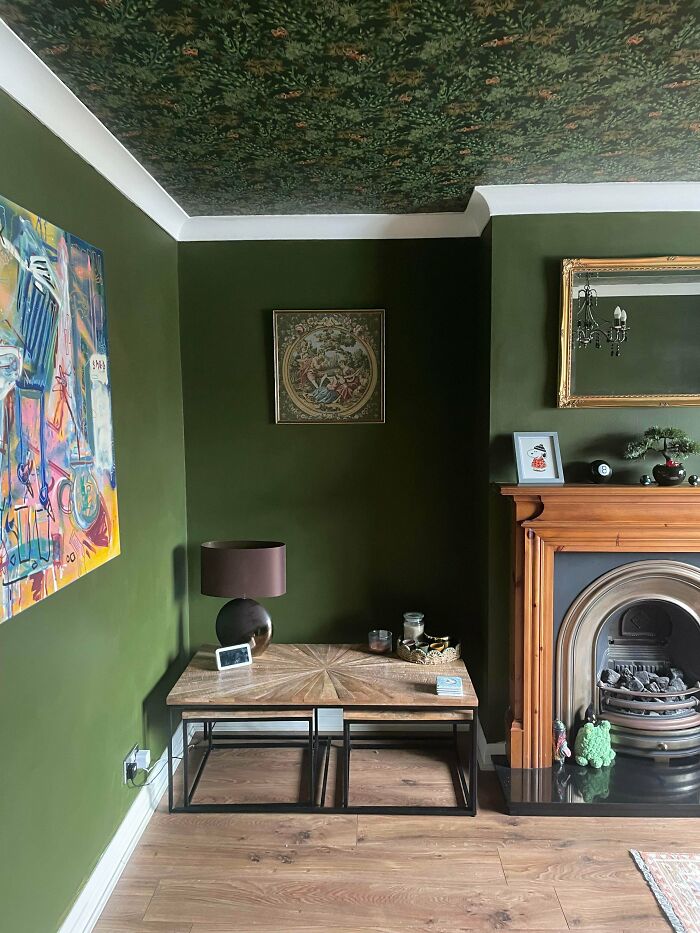 Living room with eclectic decor embracing more is more style, featuring green walls, patterned ceiling, colorful art, and ornate fireplace.