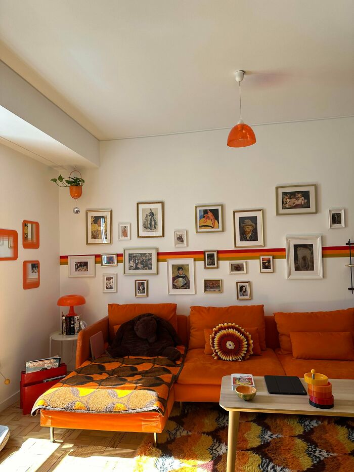 Cozy living room decked out in bold orange hues with eclectic wall art and patterned textiles embracing more is more home decor.