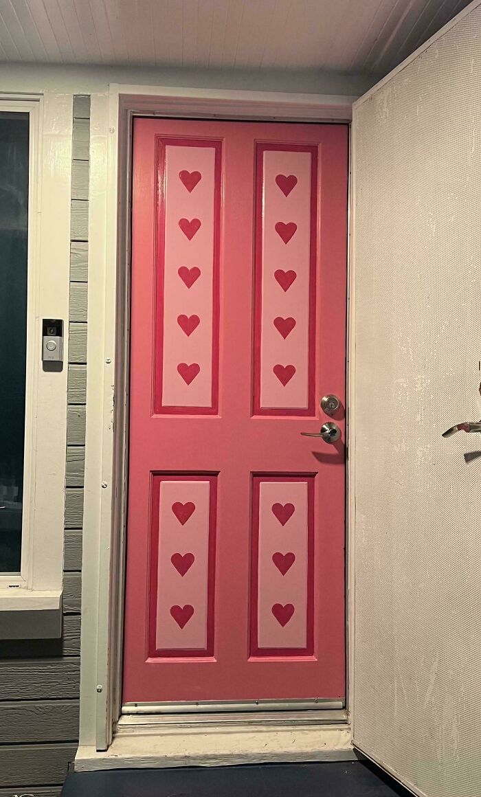 Pink front door decorated with multiple heart shapes, showcasing more is more home decor style and colorful exterior design.
