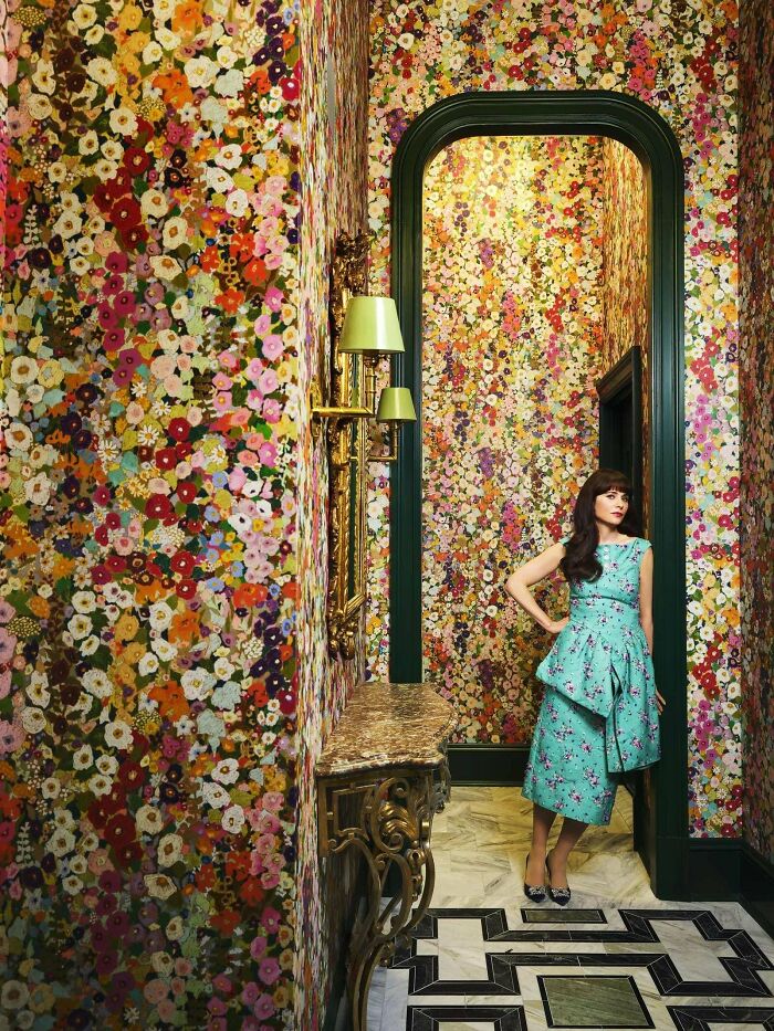 Woman in a floral dress standing in a hallway with colorful, bold floral wallpaper embracing more is more home decor.