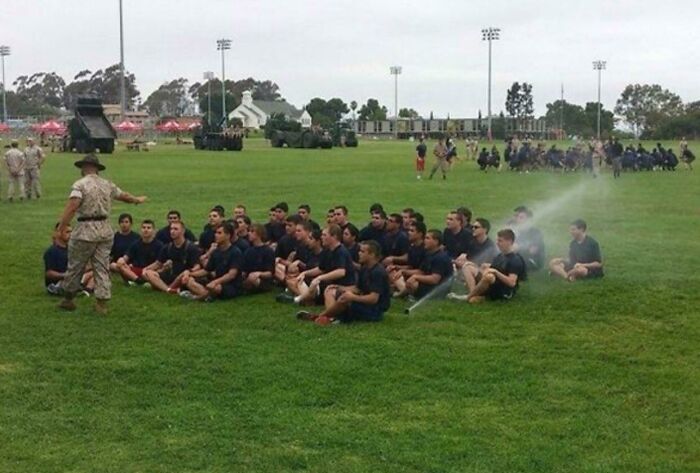Group of people sitting on grass unexpectedly sprayed by sprinklers creating a better pic than they expected.