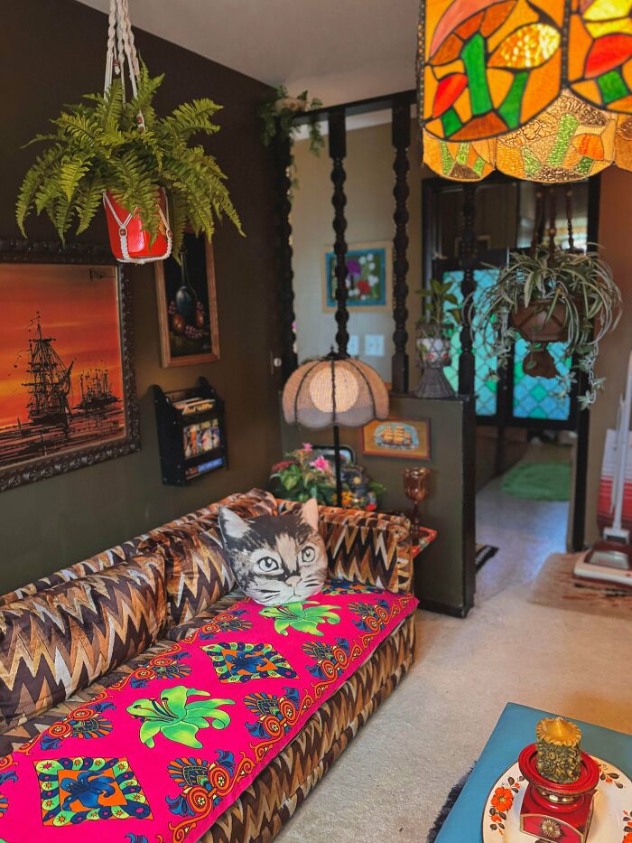Eclectic living room embracing more is more style with vibrant textiles, hanging plants, patterned couch, and artistic decor.