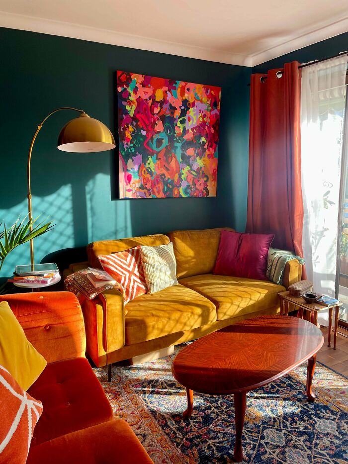Colorful living room with more is more home decor, featuring vibrant couches, bold artwork, patterned pillows, and rich curtains.