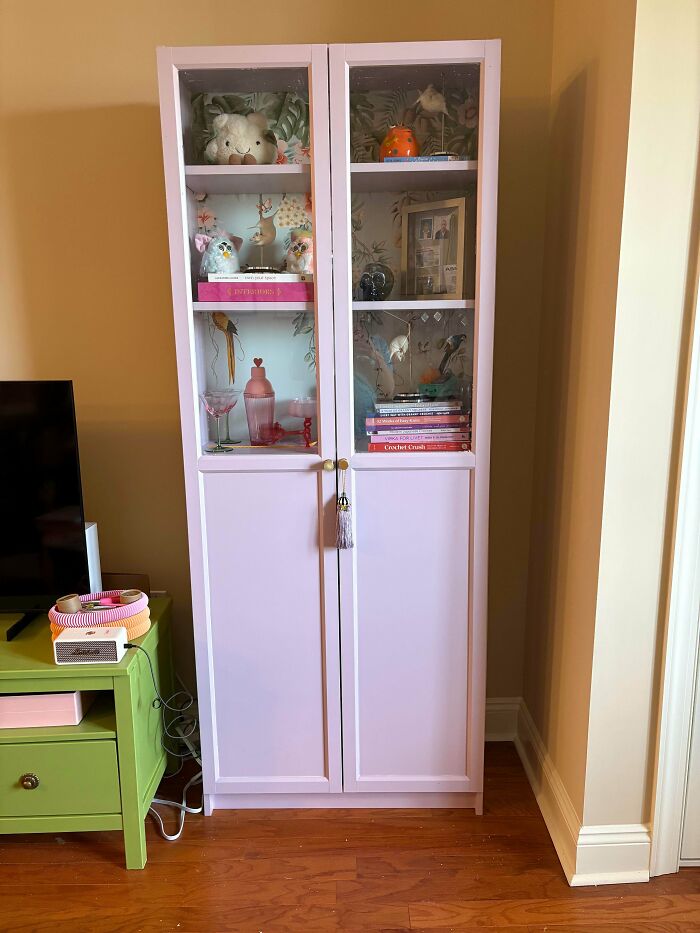 Tall white cabinet filled with colorful decor and books, showcasing a more is more home design style.