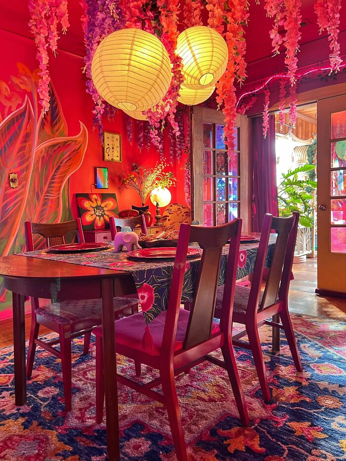 Vibrant dining room embracing more is more decor with colorful patterns, floral accents, hanging lanterns, and eclectic furniture.