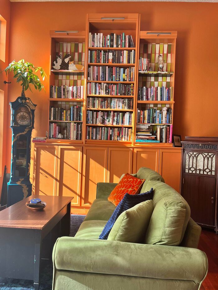 Cozy living room with vibrant orange walls, a green sofa, colorful pillows, and a large bookshelf filled with books.