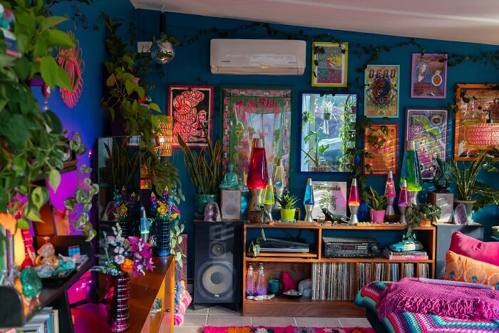 Colorful living room decked out with vibrant plants, lava lamps, and eclectic wall art showcasing more is more home decor.