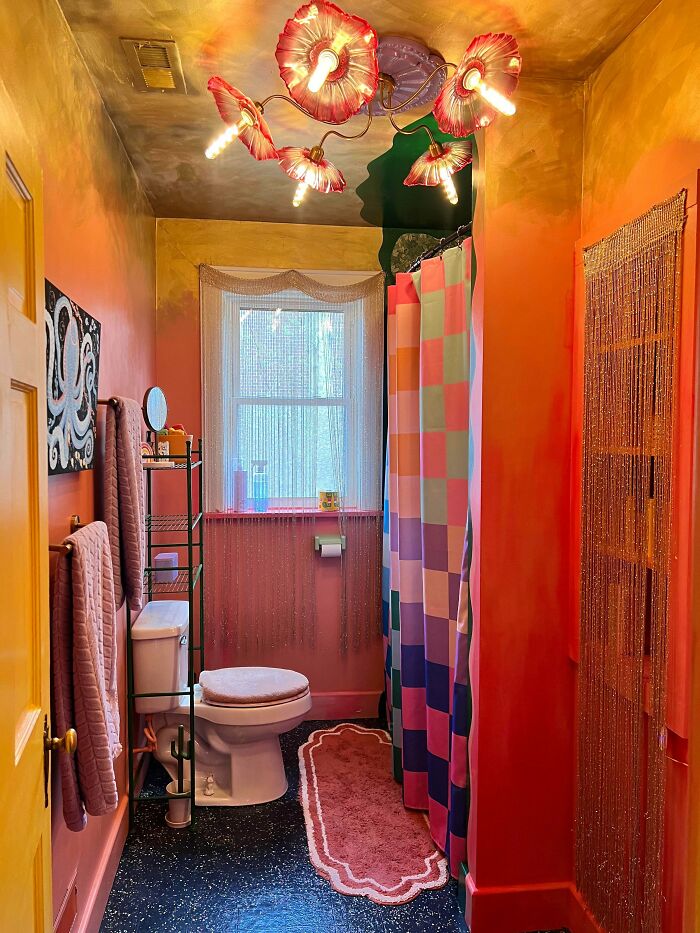 Colorful bathroom featuring bold lighting, patterned shower curtain, and layered decor showcasing more is more home design style.