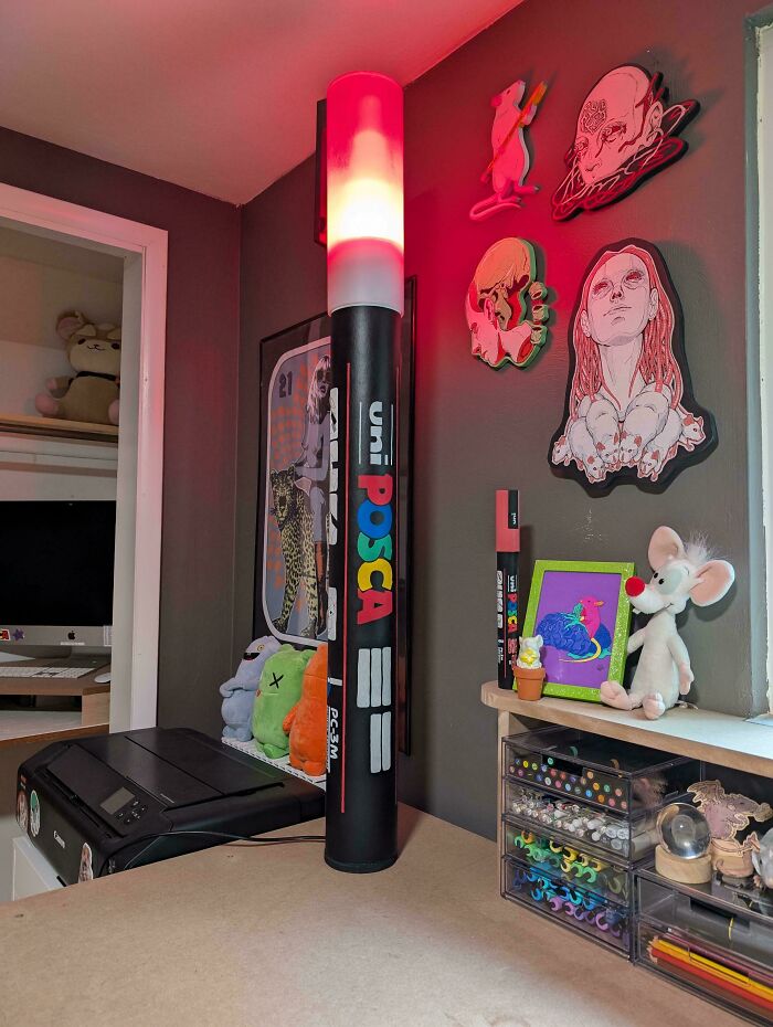 Eclectic home workspace with colorful wall art and a large illuminated uni POSCA marker lamp, embracing more is more decor.