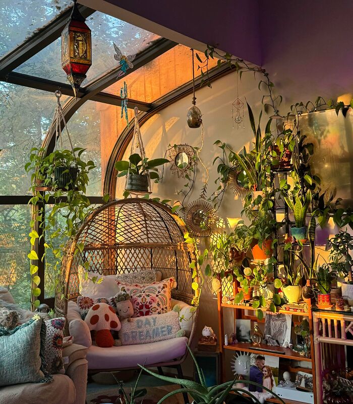 Cozy home interior filled with abundant plants, decorative pillows, hanging lanterns, and eclectic bohemian decor embracing more is more style.