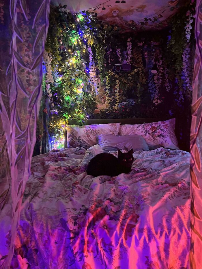 Cozy bedroom decked out with abundant greenery, floral patterns, and colorful lights embracing more is more home decor style.