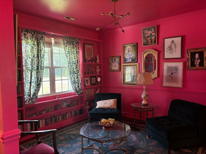 Bright pink living room with eclectic wall art, patterned curtains, and vintage furniture, showcasing a more is more home decor style.