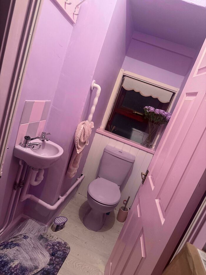 Small bathroom decked out in purple with floral accents and bold colorful decor embracing more is more home style.