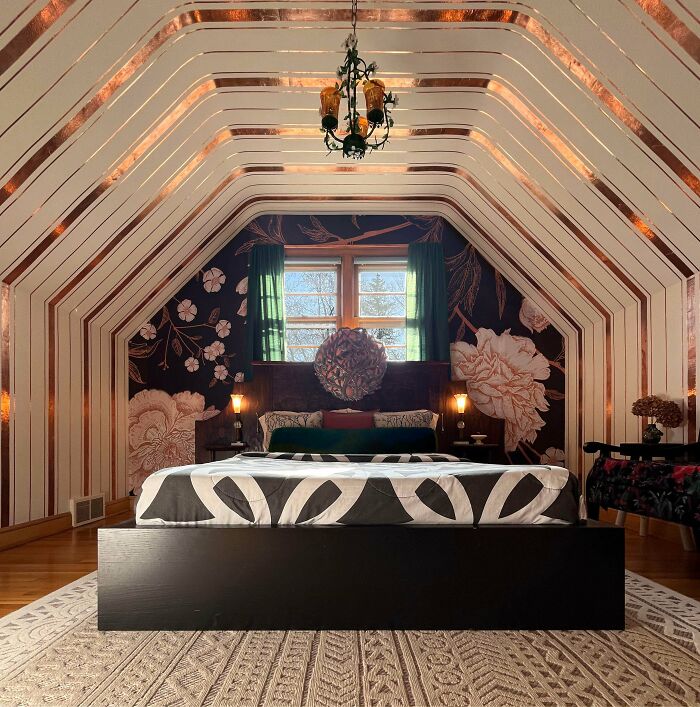 Eclectic bedroom showcasing more is more home decor with floral wallpaper, geometric bedspread, and layered lighting in an attic space.