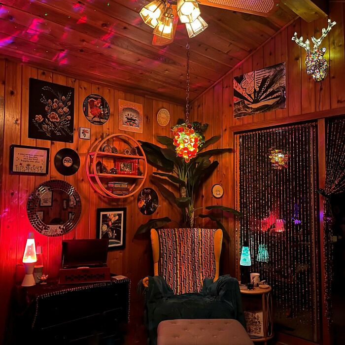 Eclectic home interior with wood paneling, colorful lights, lava lamps, and diverse wall art embracing more is more decor style.