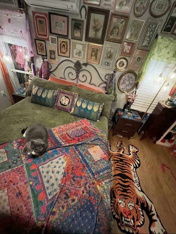 Eclectic bedroom with vibrant patterned quilt, tiger rug, numerous framed artworks, and a cat resting on the bed showcasing more is more home decor.