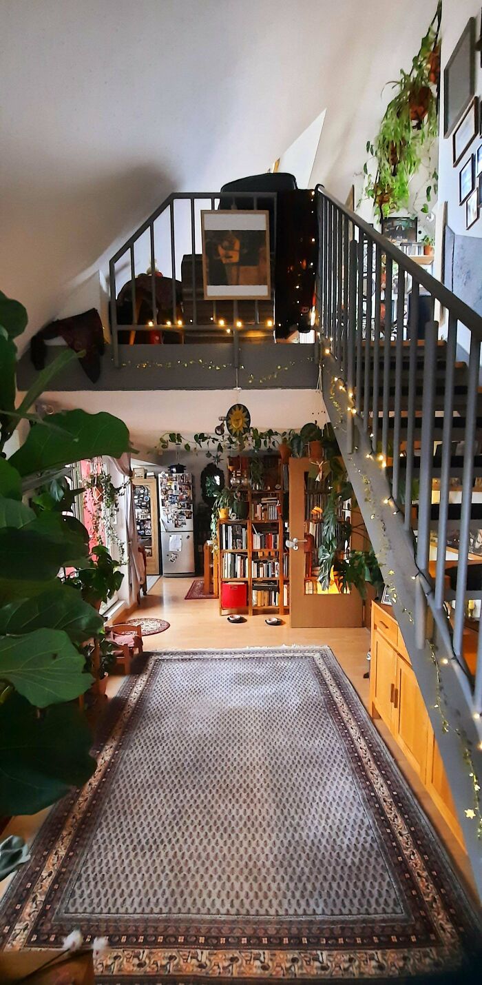 Cozy home interior richly decorated with plants, bookshelves, and fairy lights embracing more is more home decor style.