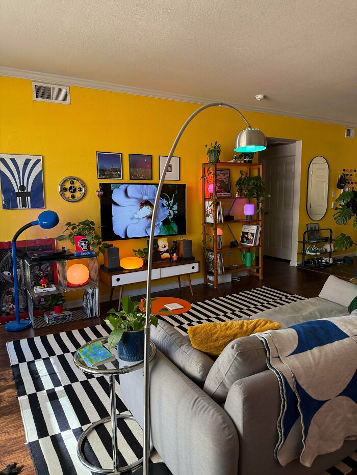 Living room embracing more is more decor style with bright yellow walls, colorful lamps, plants, and eclectic furniture arrangement.